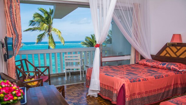 Una habitación con una cama, una mesa con un florero, una silla y vista al océano.