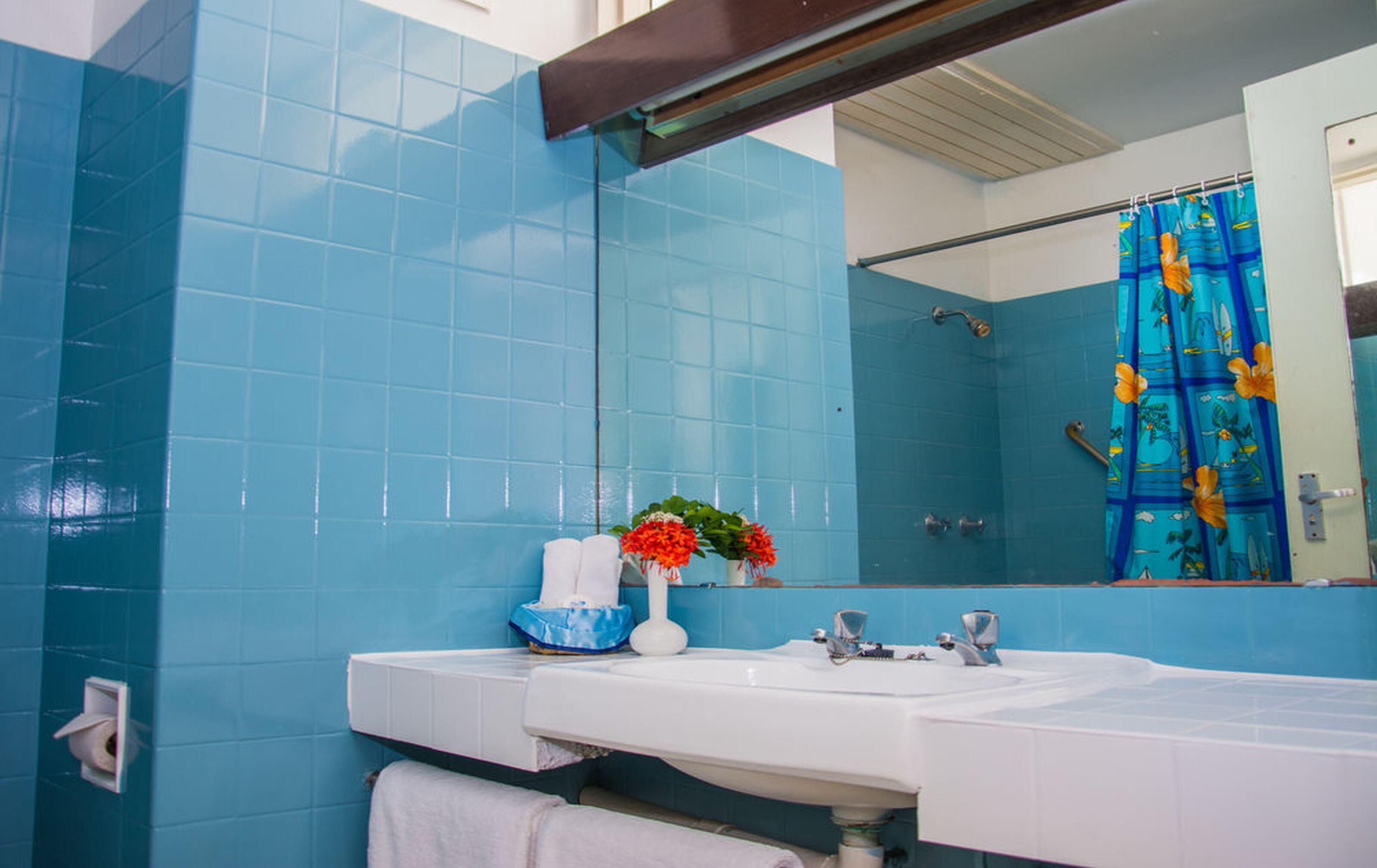 A bathroom with blue tiles, a white sink, a mirror, and a shower curtain with a tropical design.