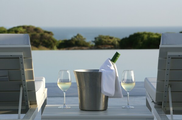 A table with a champagne bottle, two glasses, and a bucket, overlooking a scenic view of the sea and greenery.