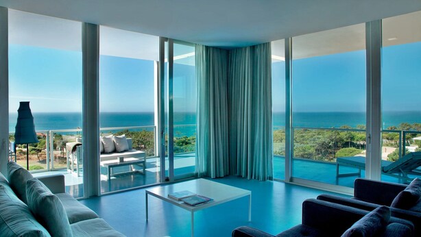 Ein modernes Wohnzimmer mit großem Balkon, weißen Möbeln und Meerblick.
