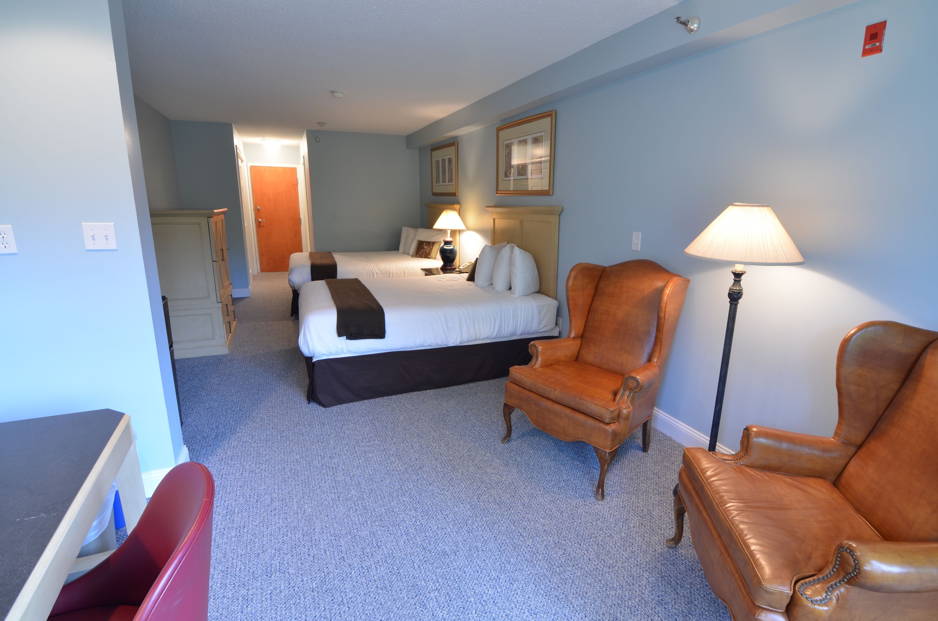 Une chambre d’hôtel avec un lit, deux chaises, un bureau et une lampe.