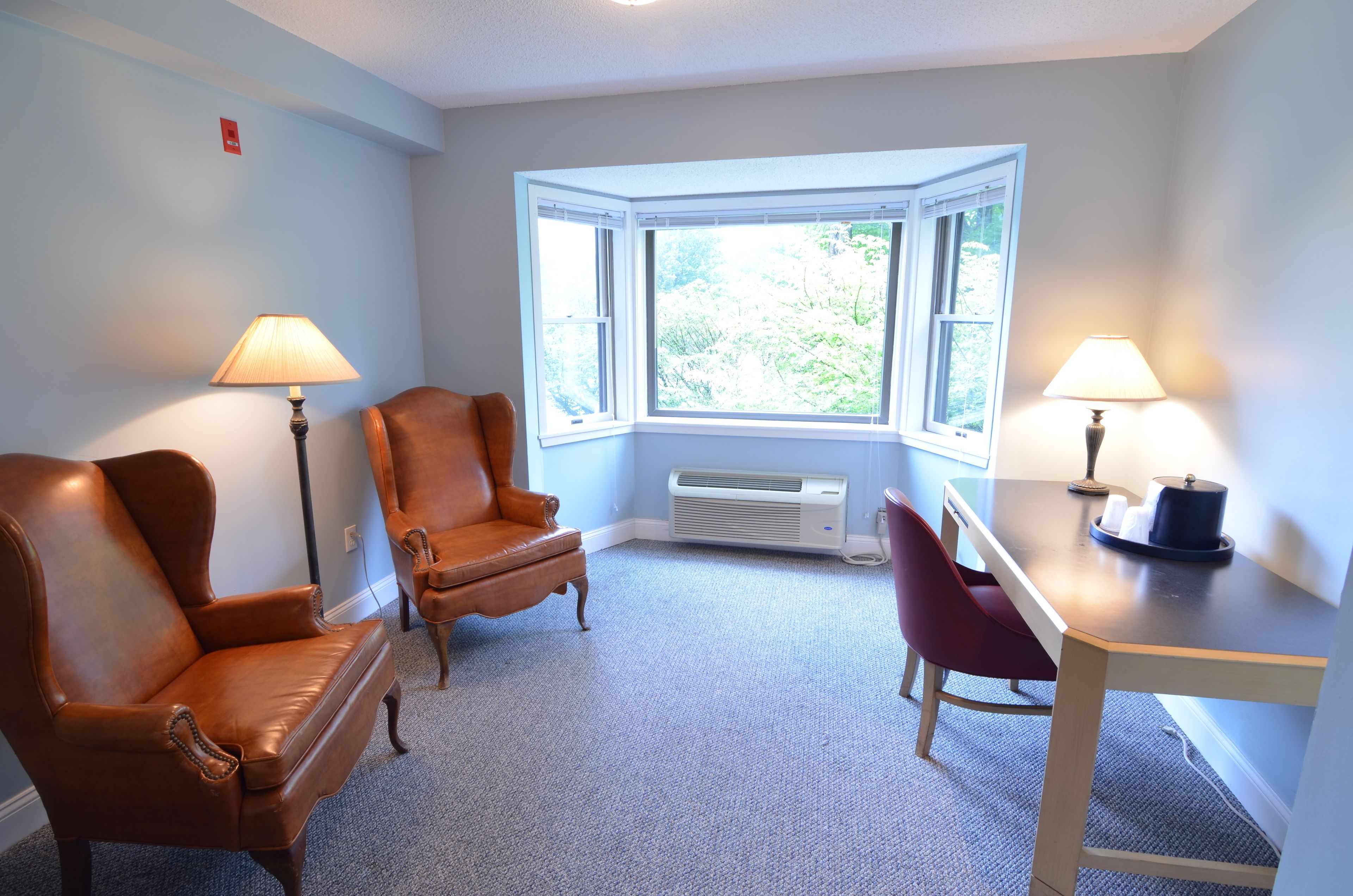 A room with two leather armchairs, a wooden table, and two lamps.
