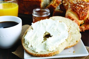 A bagel with cream cheese, a glass of orange juice, and a jar of jam on a table.