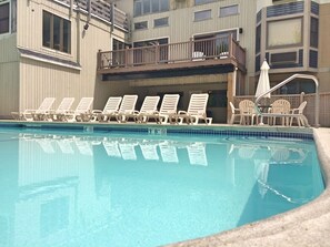 A swimming pool with lounge chairs and a building with balconies in the background.
