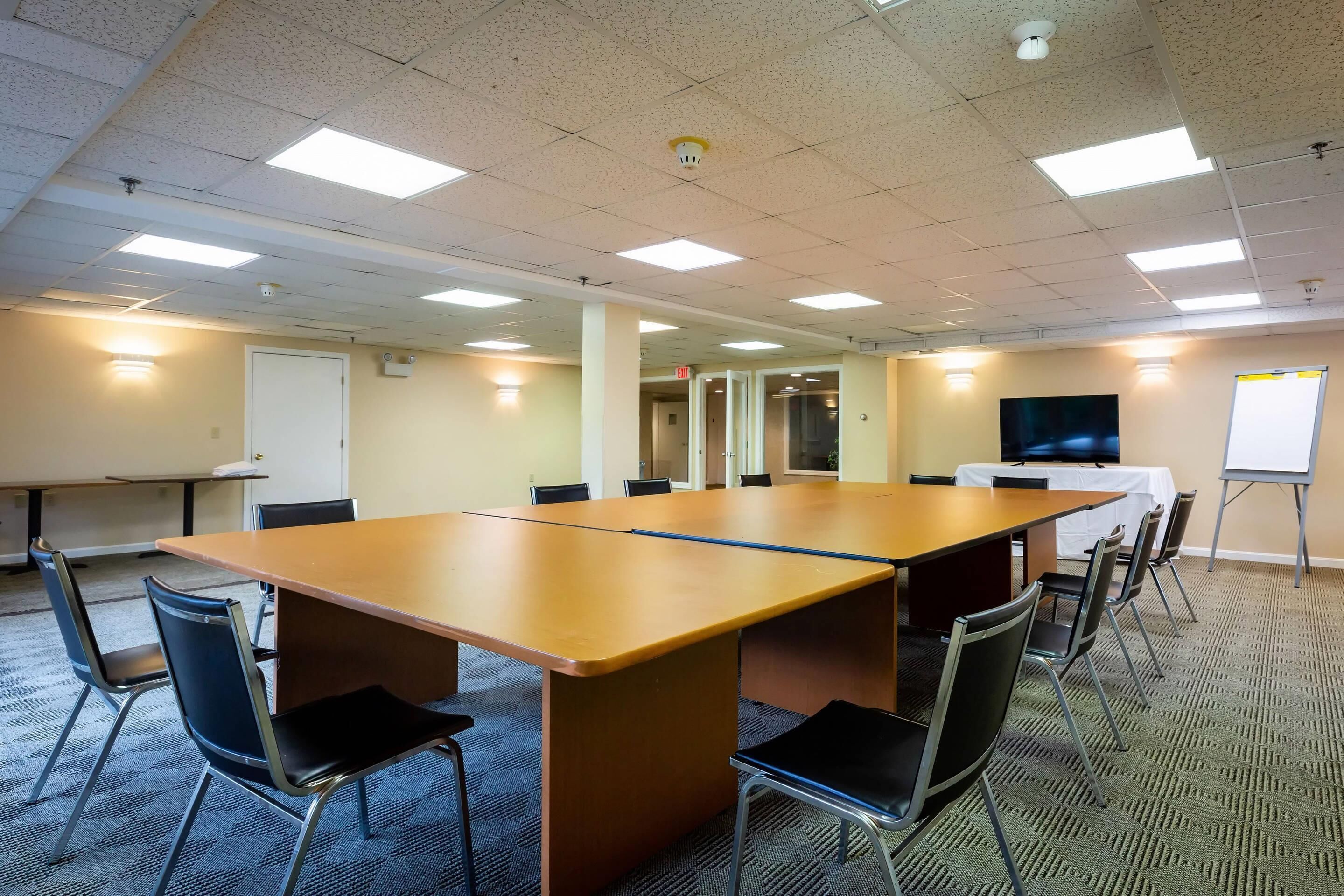 A conference room with a long table, chairs, a whiteboard, and a TV.