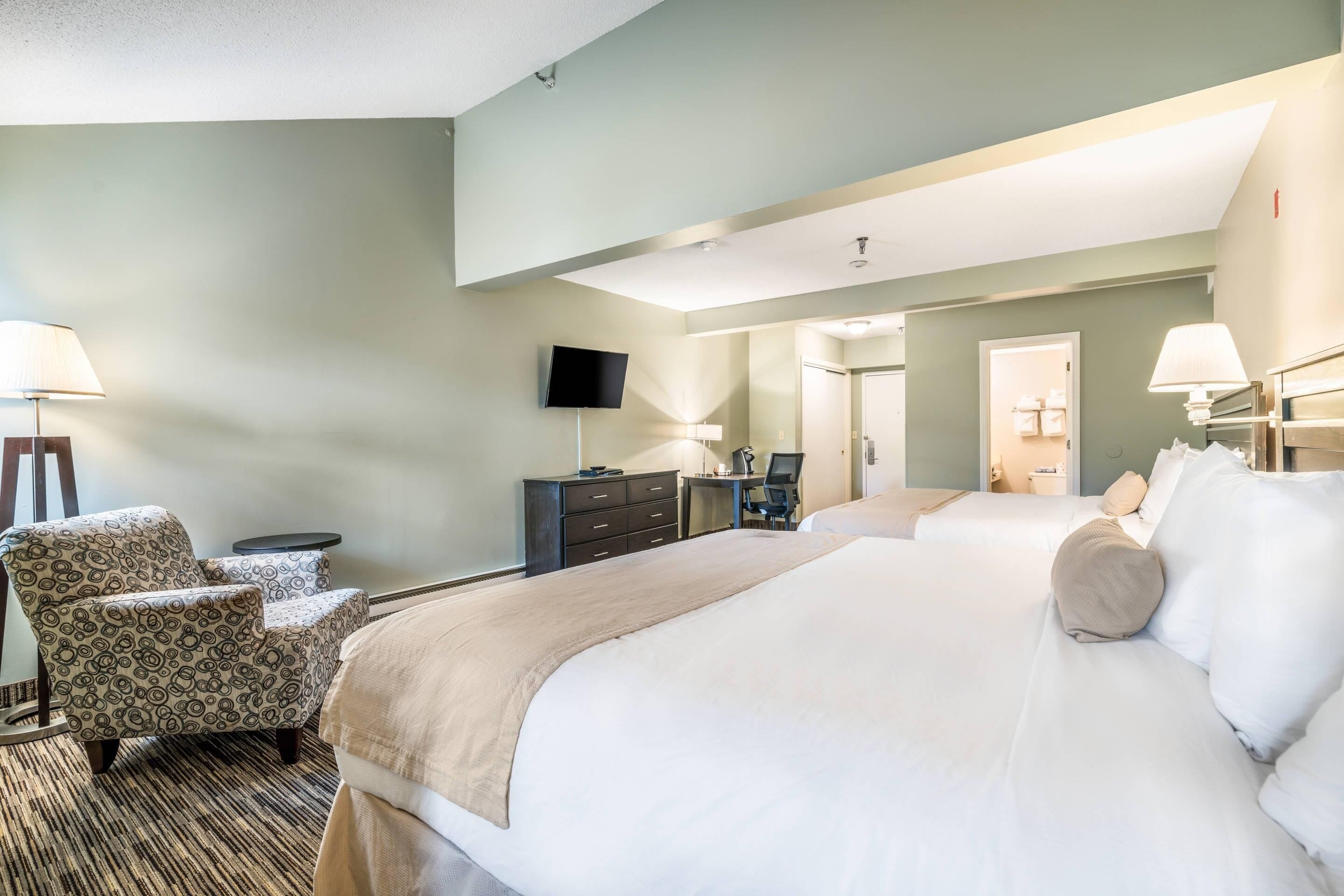 Une chambre d’hôtel avec deux lits, un bureau, une chaise, une télévision et une lampe.