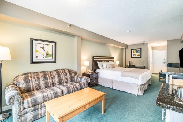A hotel room with a bed, a sofa, a desk, and a lamp.