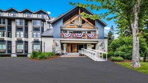 A multi-story hotel with a stone facade, a balcony with a railing, and a flag display. - The Valley Inn, an Ascend Collection Hotel (Waterville Valley)