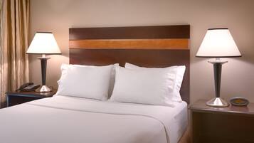 A hotel room with a bed, two bedside lamps, a nightstand with a phone, and a digital clock.