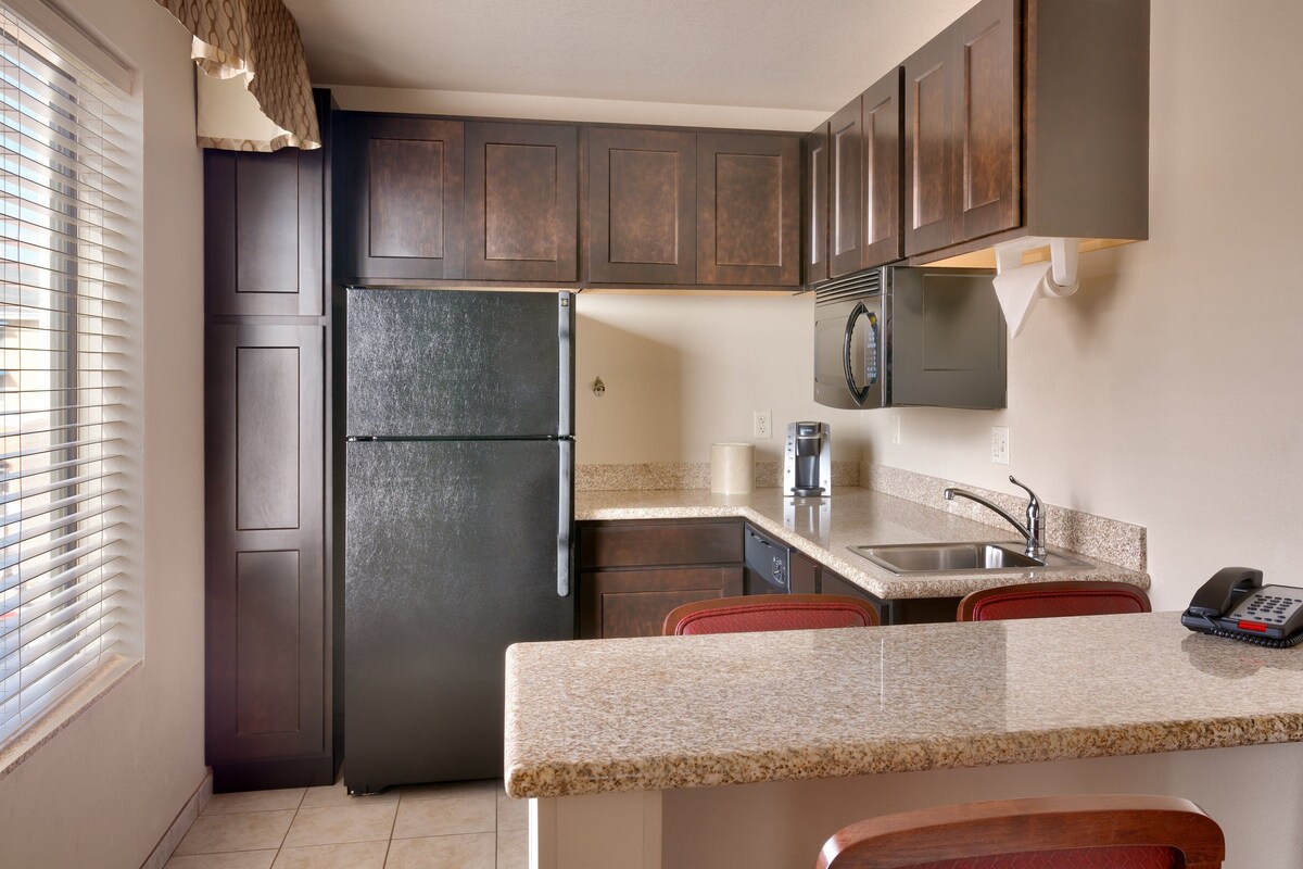 A compact kitchen with dark wood cabinets, a stainless steel refrigerator, a microwave, and a sink with a telephone.