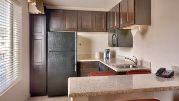 A compact kitchen with dark wood cabinets, a stainless steel refrigerator, a microwave, and a sink with a telephone.