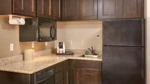 A kitchen with dark wooden cabinets, a black microwave, a black refrigerator, a granite countertop, and a coffee maker. - Holiday Inn Express & Suites Orem-North Provo by IHG (Orem)