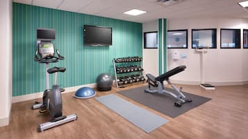 Une salle de sport équipée de matériel d’exercice, d’un téléviseur et d’une horloge murale.