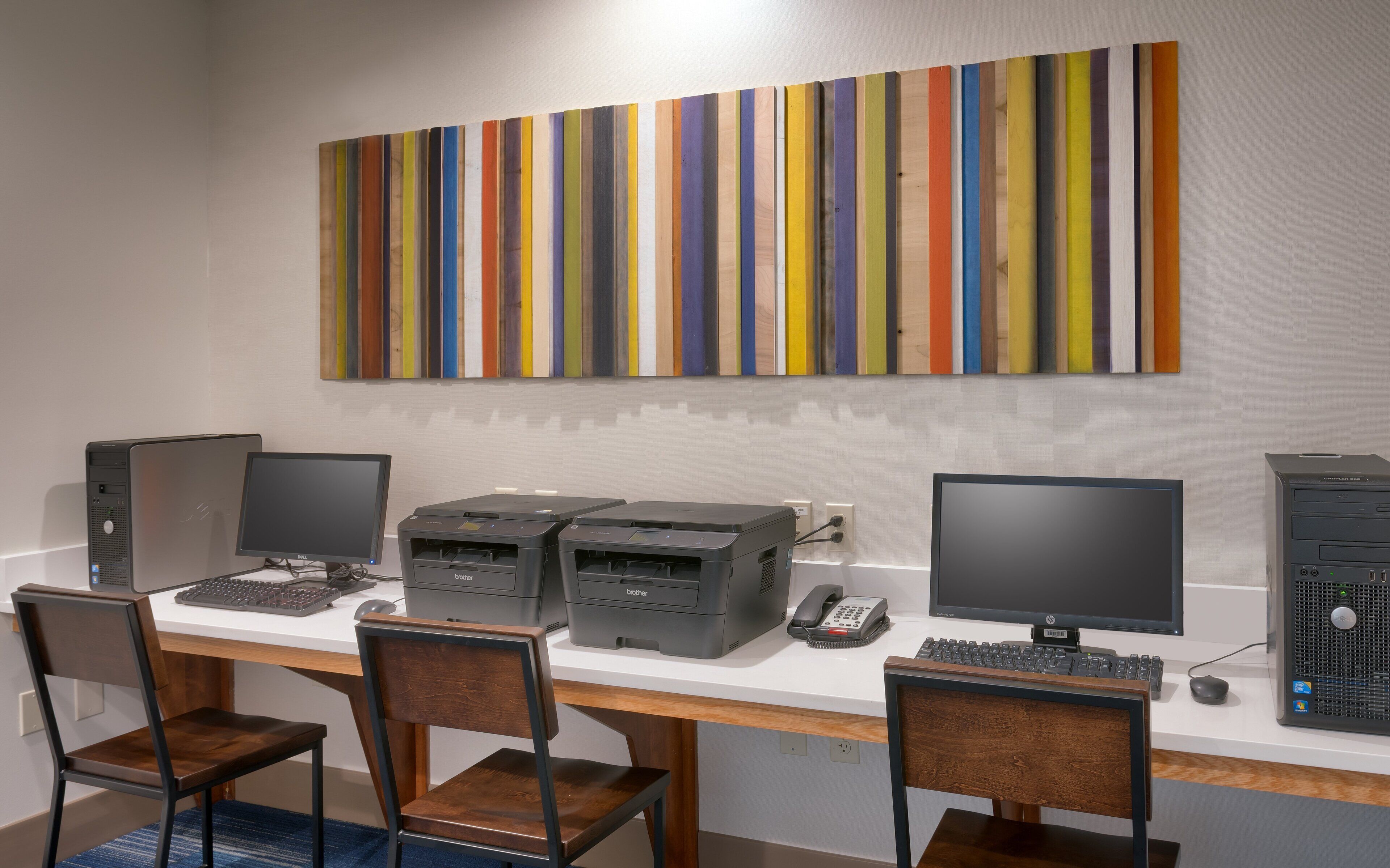 Ein Arbeitsplatz mit zwei Desktop-Computern, zwei Druckern und zwei Stühlen.