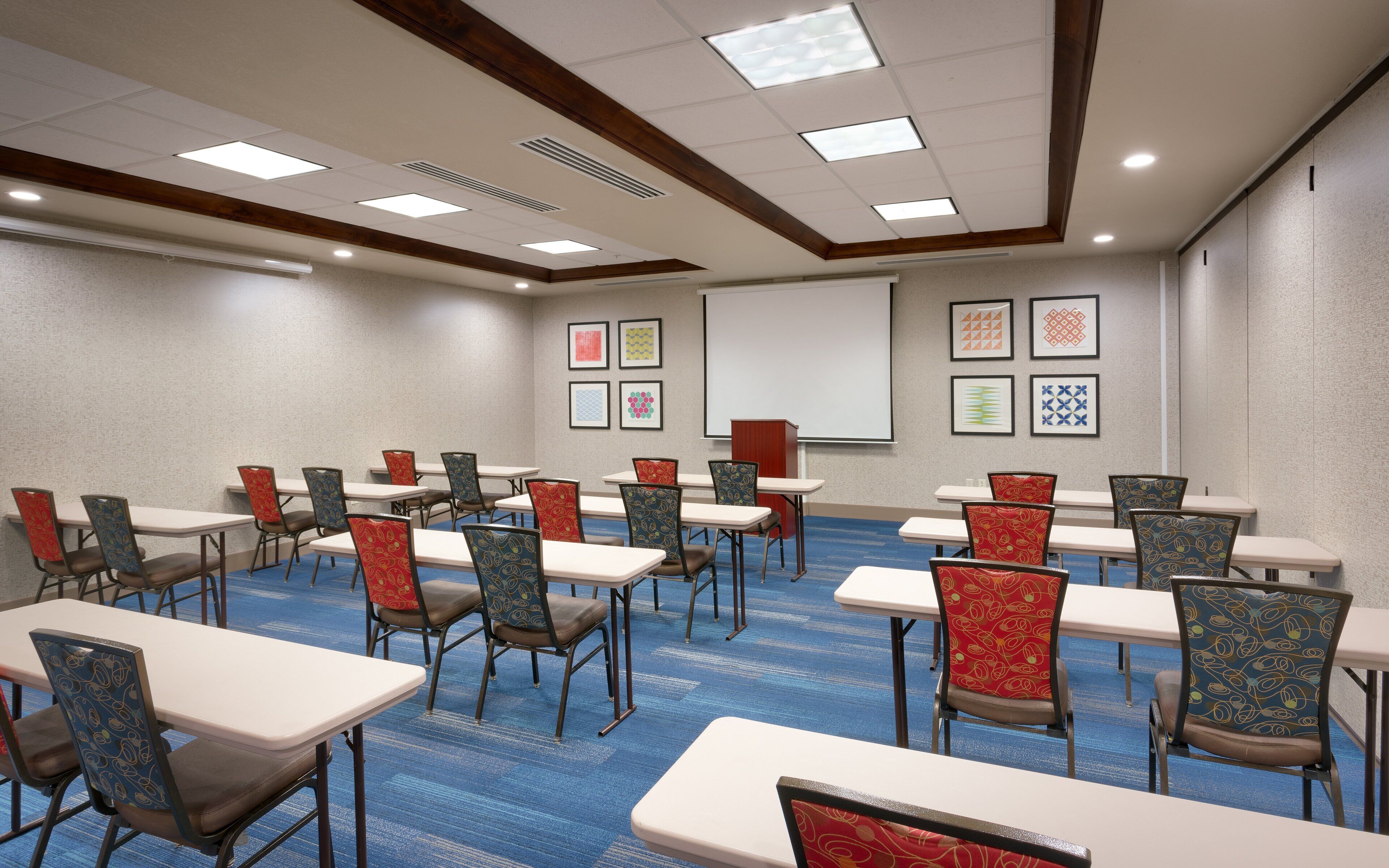 A conference room with tables and chairs, a projector screen, and framed artwork on the walls.
