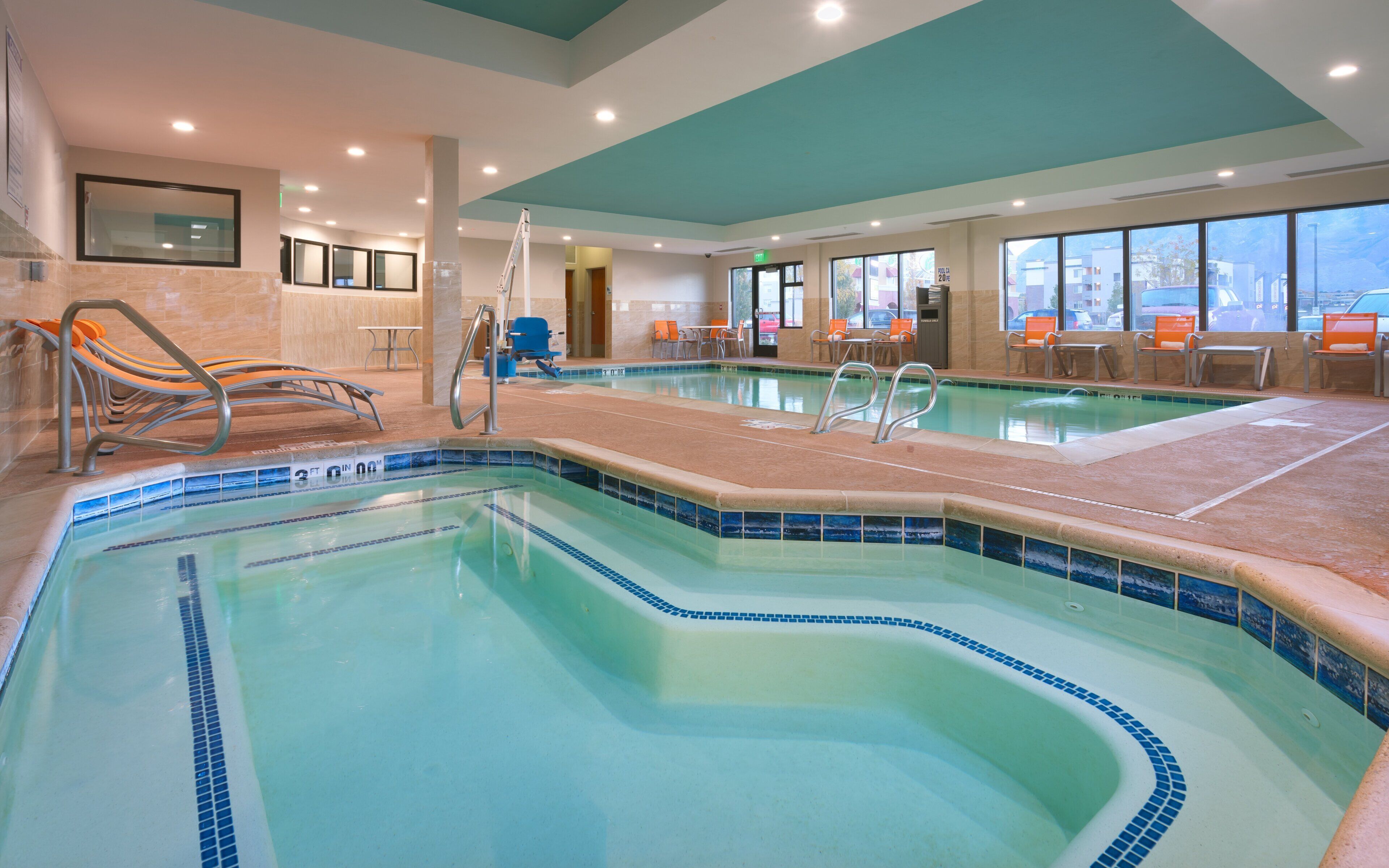 A swimming pool with a tiled edge, a ladder, and seating areas with chairs.