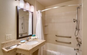 Une salle de bain avec un lavabo doté d’un plan de travail en granit, un miroir, une douche avec un pommeau de douche amovible et un porte-serviettes.