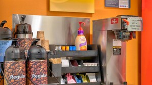 Una estación de café con dos dispensadores de café etiquetados como “Regular”, una botella de café Folgers y una máquina de café.