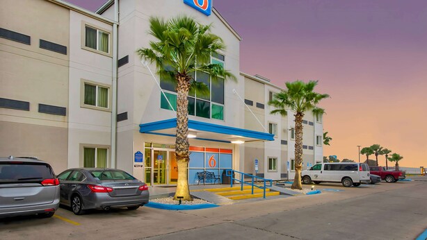 Un motel con un llamativo letrero con el número '6', un estacionamiento y palmeras.