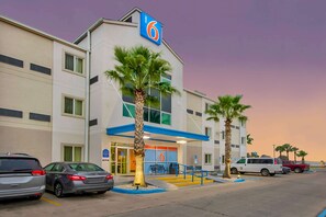 Un motel con un llamativo letrero con el número '6', un estacionamiento y palmeras.