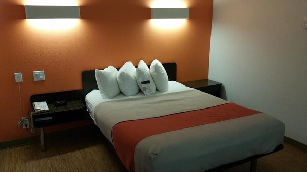 Habitación de hotel con cama, mesita de noche con teléfono y dos lámparas de pared.