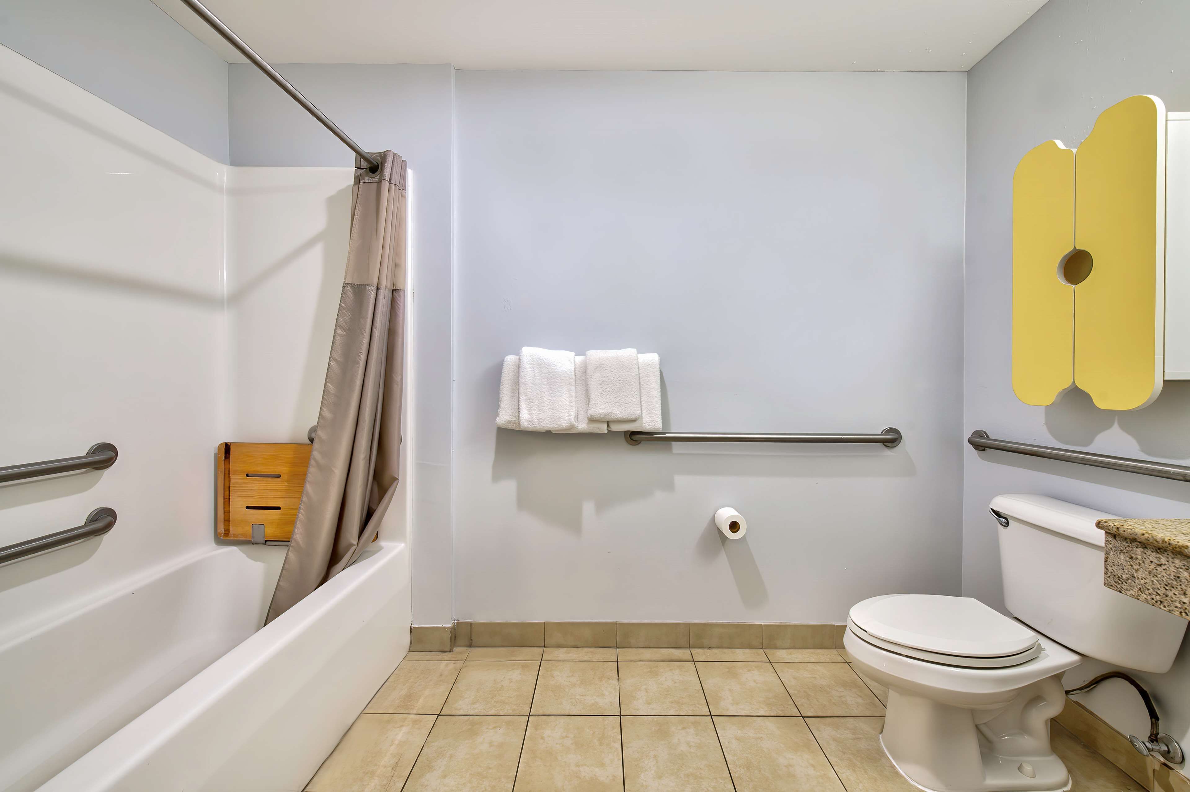 A bathroom with a bathtub, toilet, and handrails.