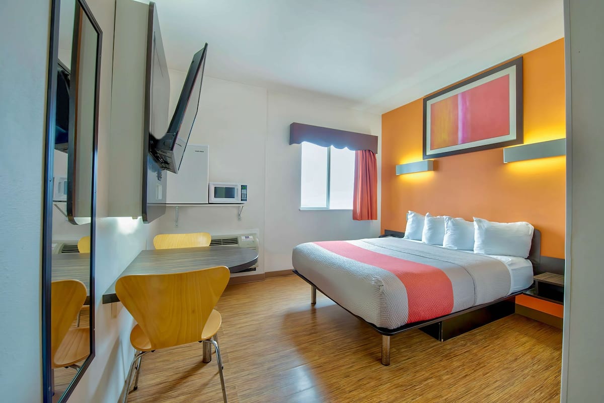 A hotel room with a bed, a desk, a chair, a TV, and a window with curtains.