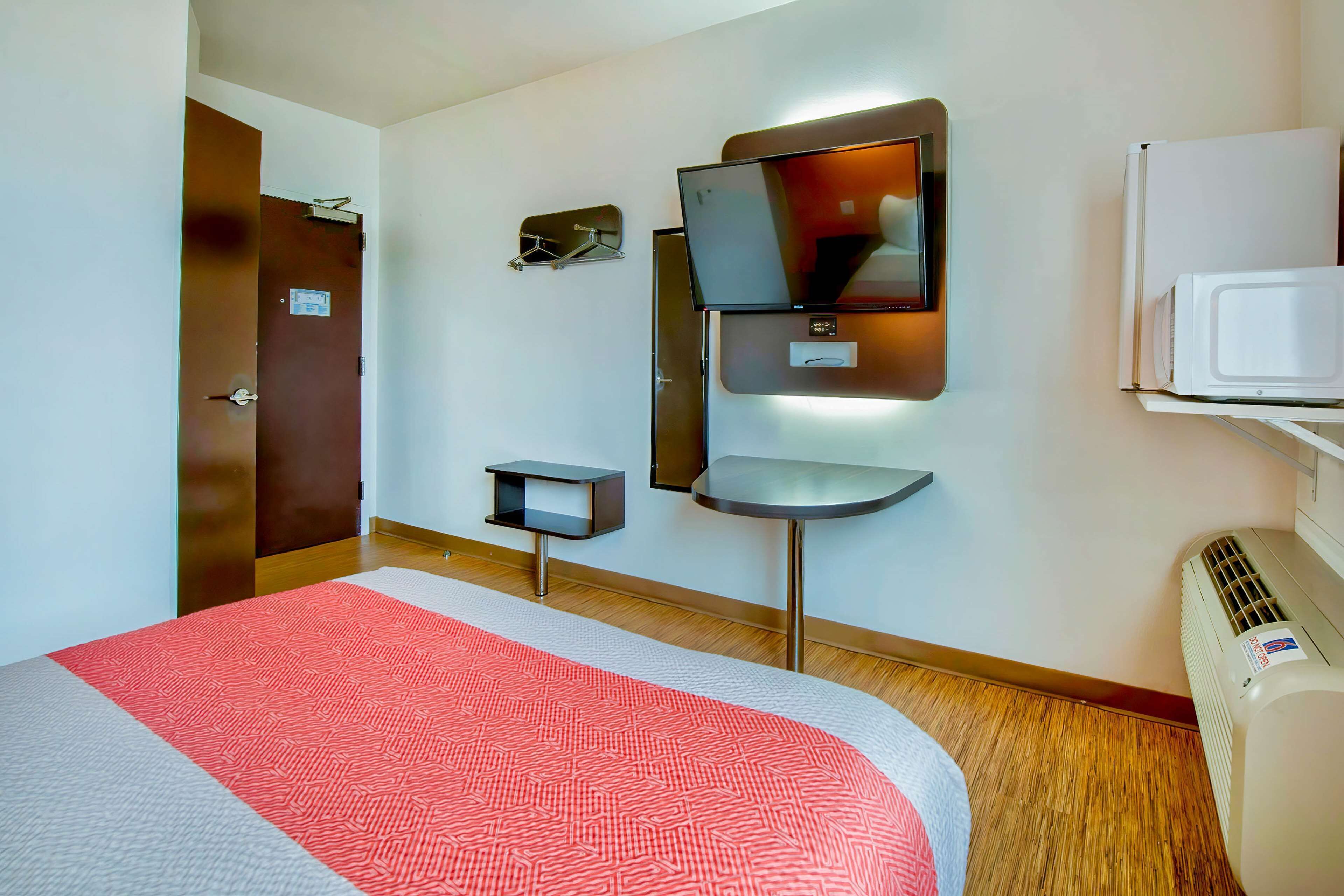 Una habitación de hotel con cama, televisor montado en la pared, una mesita y un microondas.