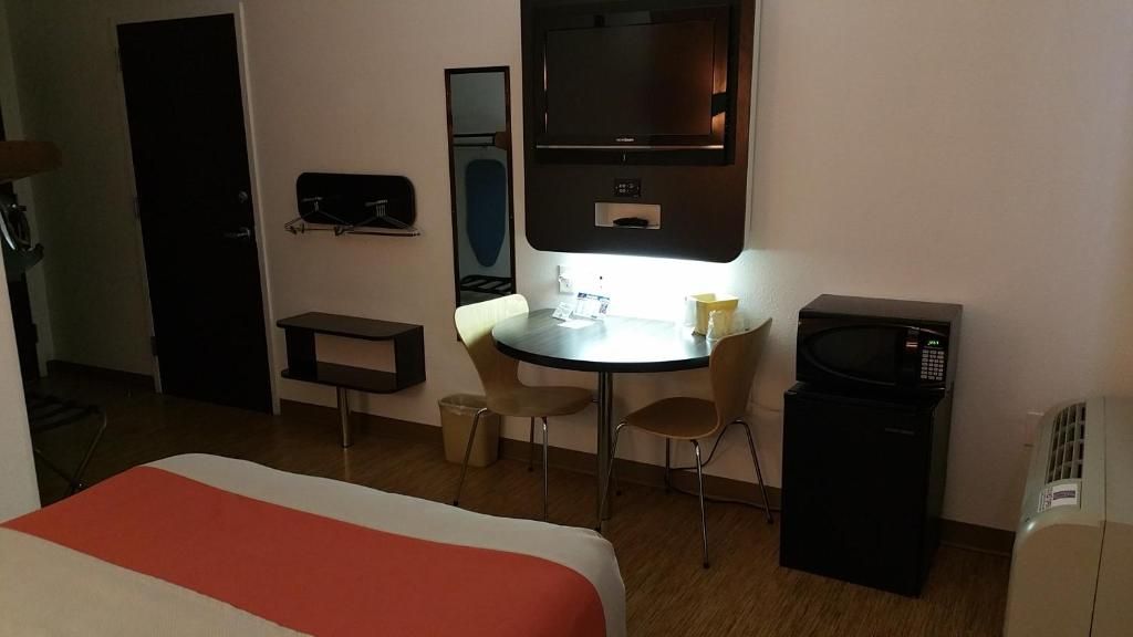Habitación de hotel con cama, escritorio, silla, microondas y un pequeño cesto de basura.