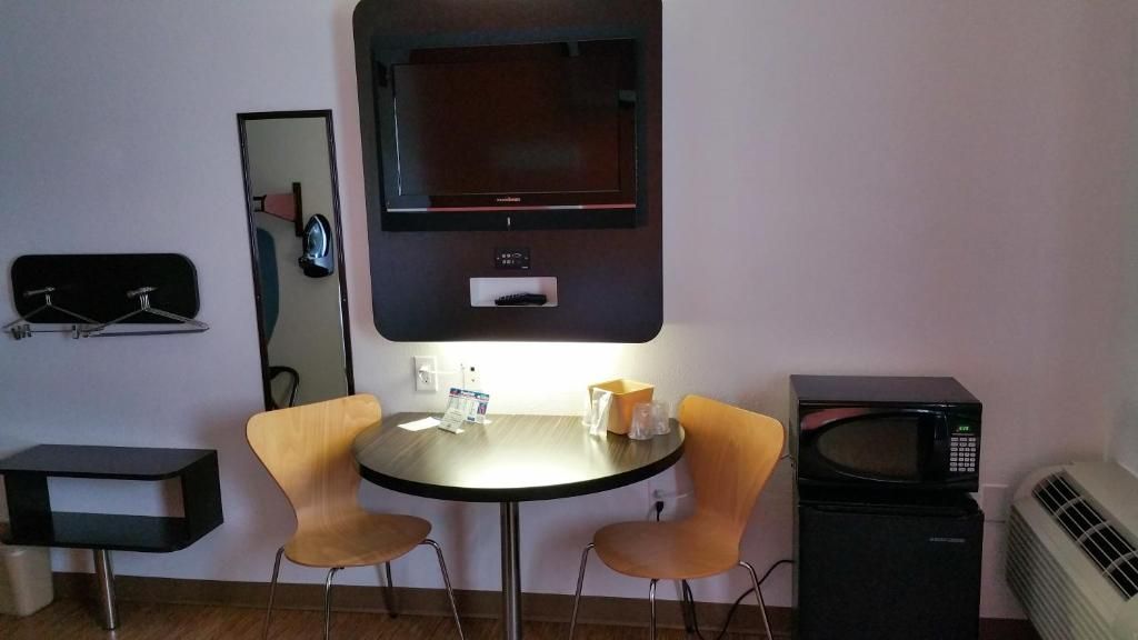 A small room with a round table, two chairs, a television, a microwave, and a mirror.