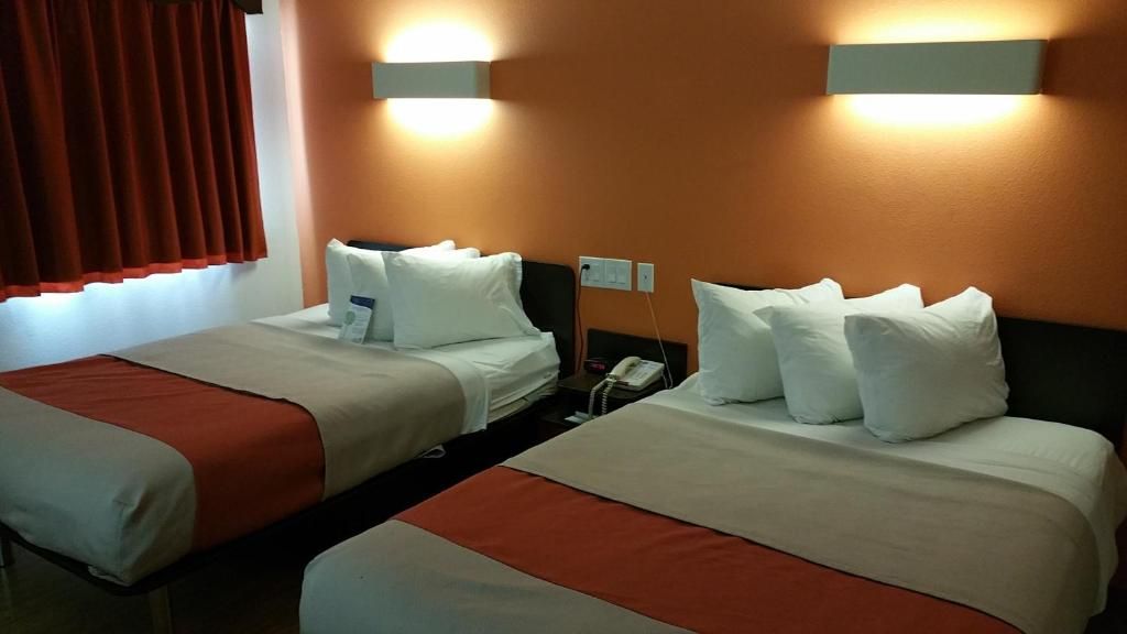 A hotel room with two beds, each with white linens and pillows, a telephone, and wall-mounted lighting.