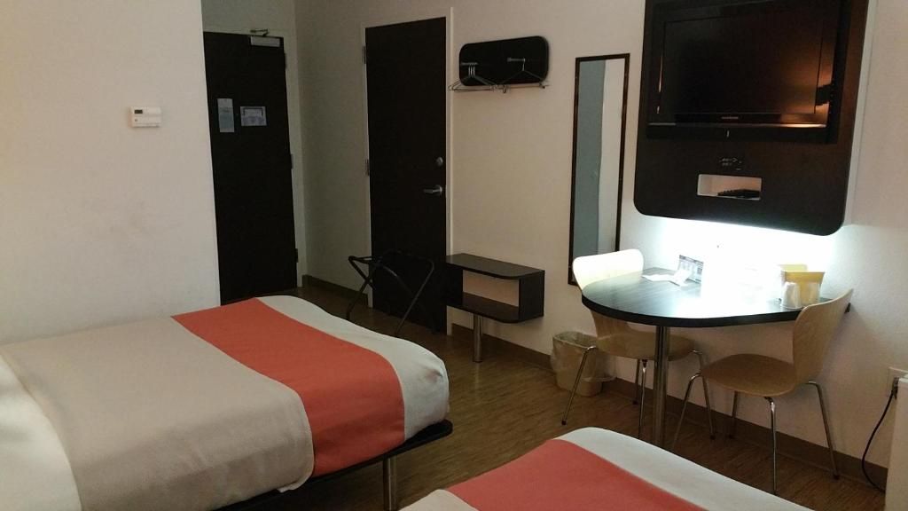 A hotel room with two beds, a desk, a chair, a television, and a small table with a cup.