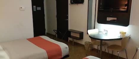 A hotel room with two beds, a desk, a chair, a television, and a small table with a cup.