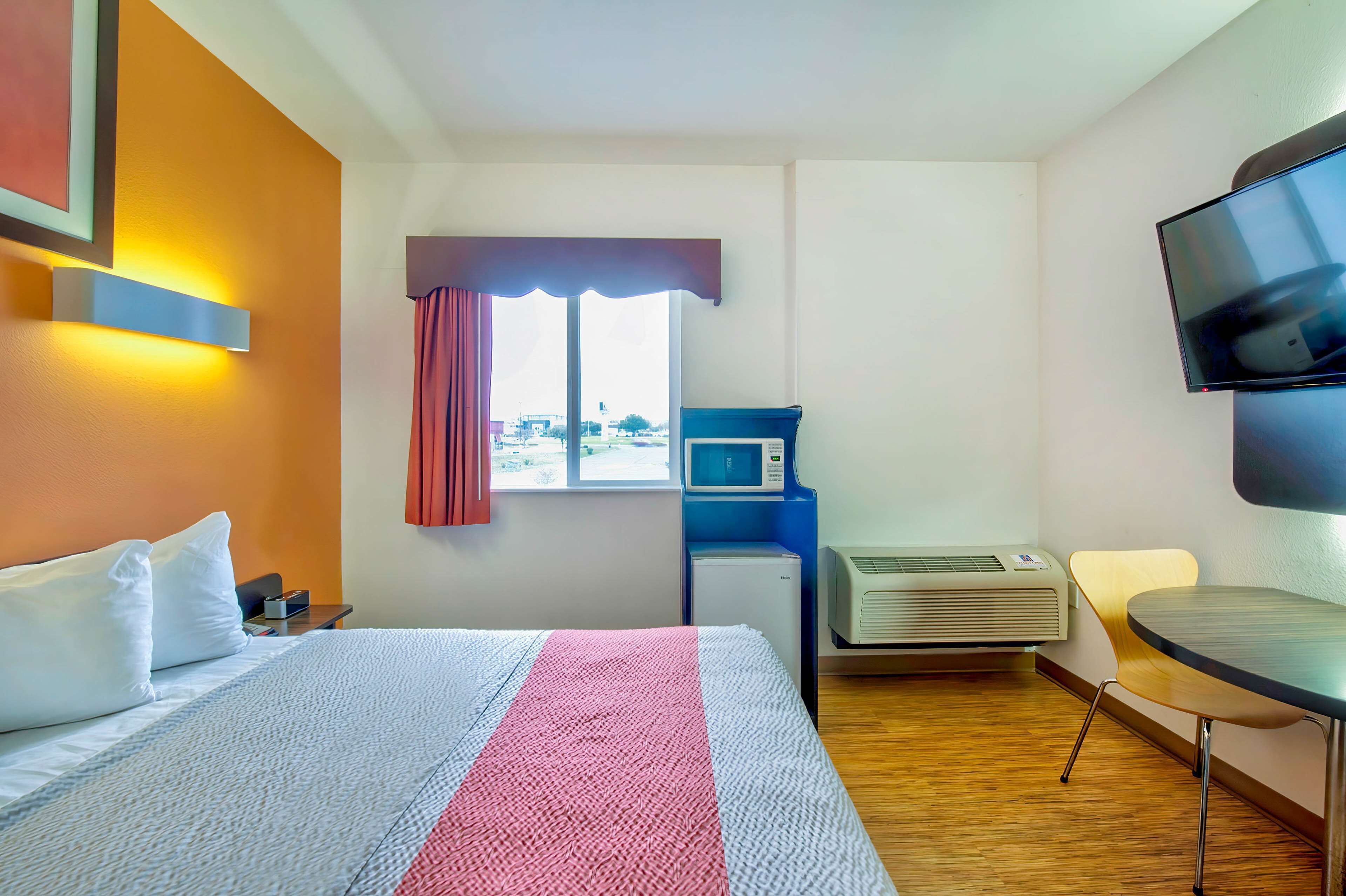 A hotel room with a bed, a desk, a TV, a microwave, and an air conditioner.