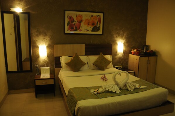 Quarto de hotel com cama bem arrumada, duas luminárias de cabeceira, mesa de cabeceira com abajur, quadro com flores na parede e um espelho.