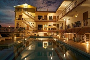 A multi-story hotel with a central courtyard pool, balconies, and a well-lit facade. - Hotel Mamallaa Heritage (Tirukalukundram)