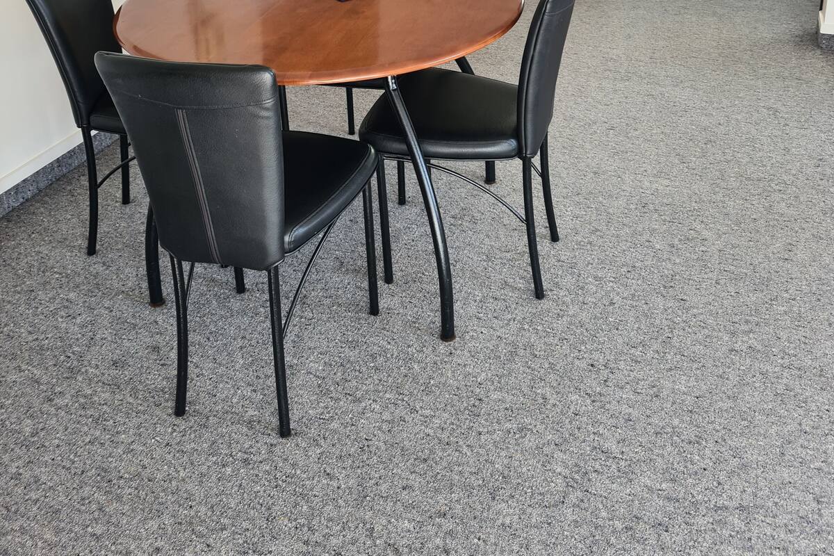 A compact kitchen with a microwave, a coffee maker, and a sink. There is a dining area with a round table and four chairs. The room has a carpeted floor and a door leading to a bathroom.
