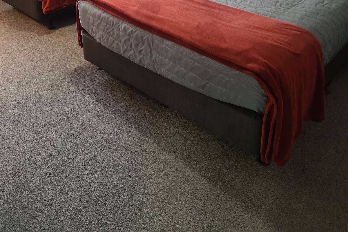 A hotel room with two beds, each with a grey and orange bedspread, and a window with sheer curtains.