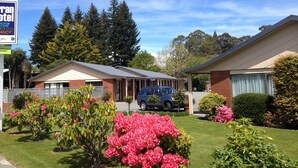 Un motel composé de deux bâtiments, d’un parking et d’un jardin agrémenté de fleurs roses.