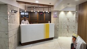 Een hotel receptie met een marmeren muur, een receptiebalie en een digitaal scherm.