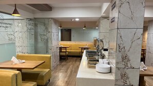 Een restaurant met marmeren wandtegels, houten vloeren, gele gestoffeerde zithoeken en een buffet.