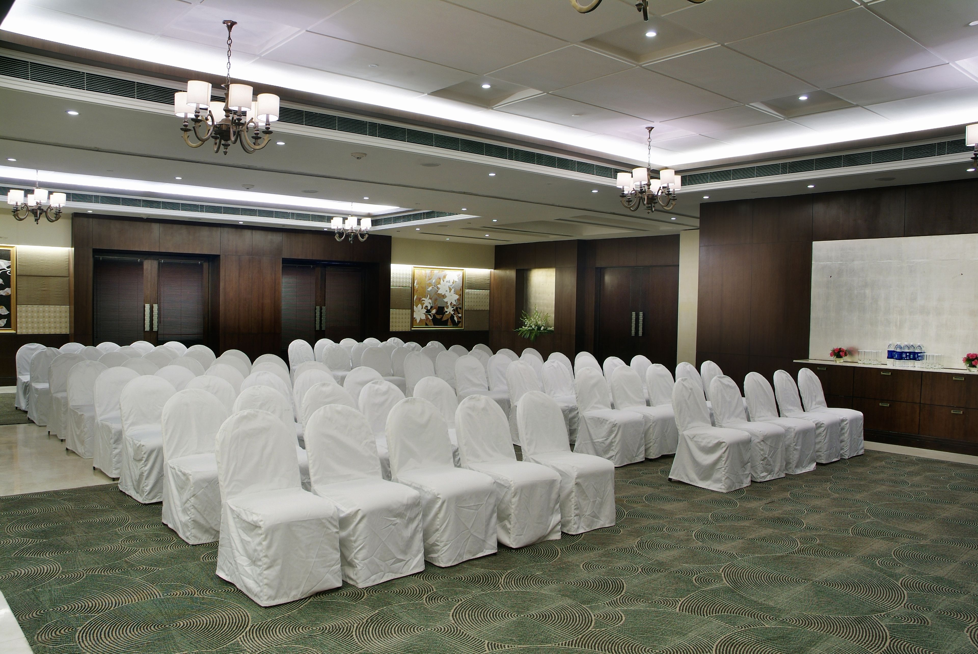 A conference room with rows of white-covered chairs, a whiteboard, and a reception desk.