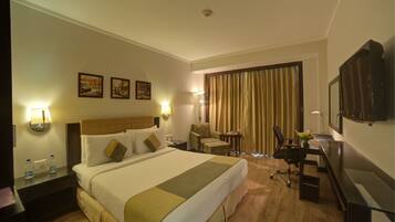A hotel room with a large bed, a desk, a chair, a TV, and two wall-mounted lamps.