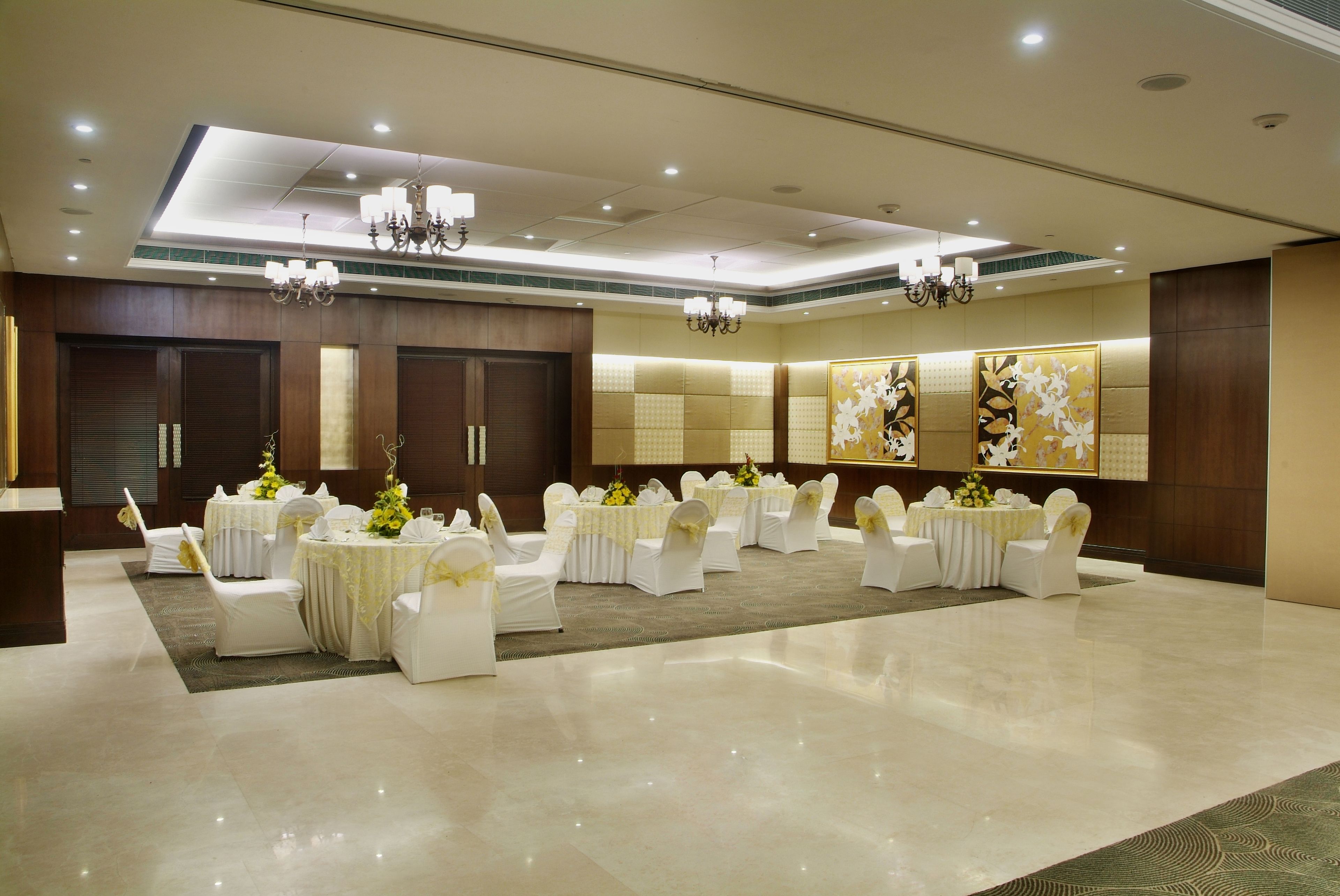 A spacious banquet hall with round tables and white chairs, chandeliers, and floral centerpieces.
