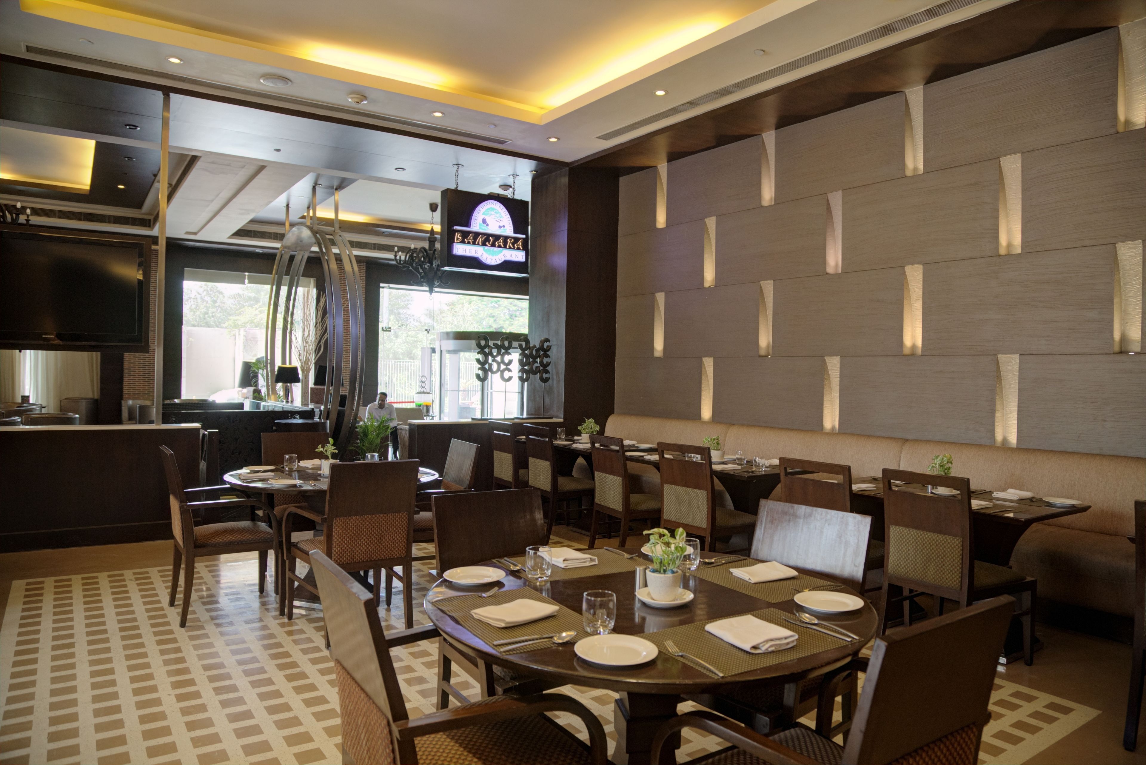Un ristorante con diversi tavoli e sedie, una zona cucina e un grande schermo televisivo.