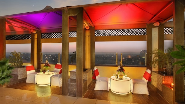 A rooftop terrace with outdoor seating, a view of the cityscape, and a sunset in the background. - Goldfinch Hotel Delhi NCR (Faridabad)