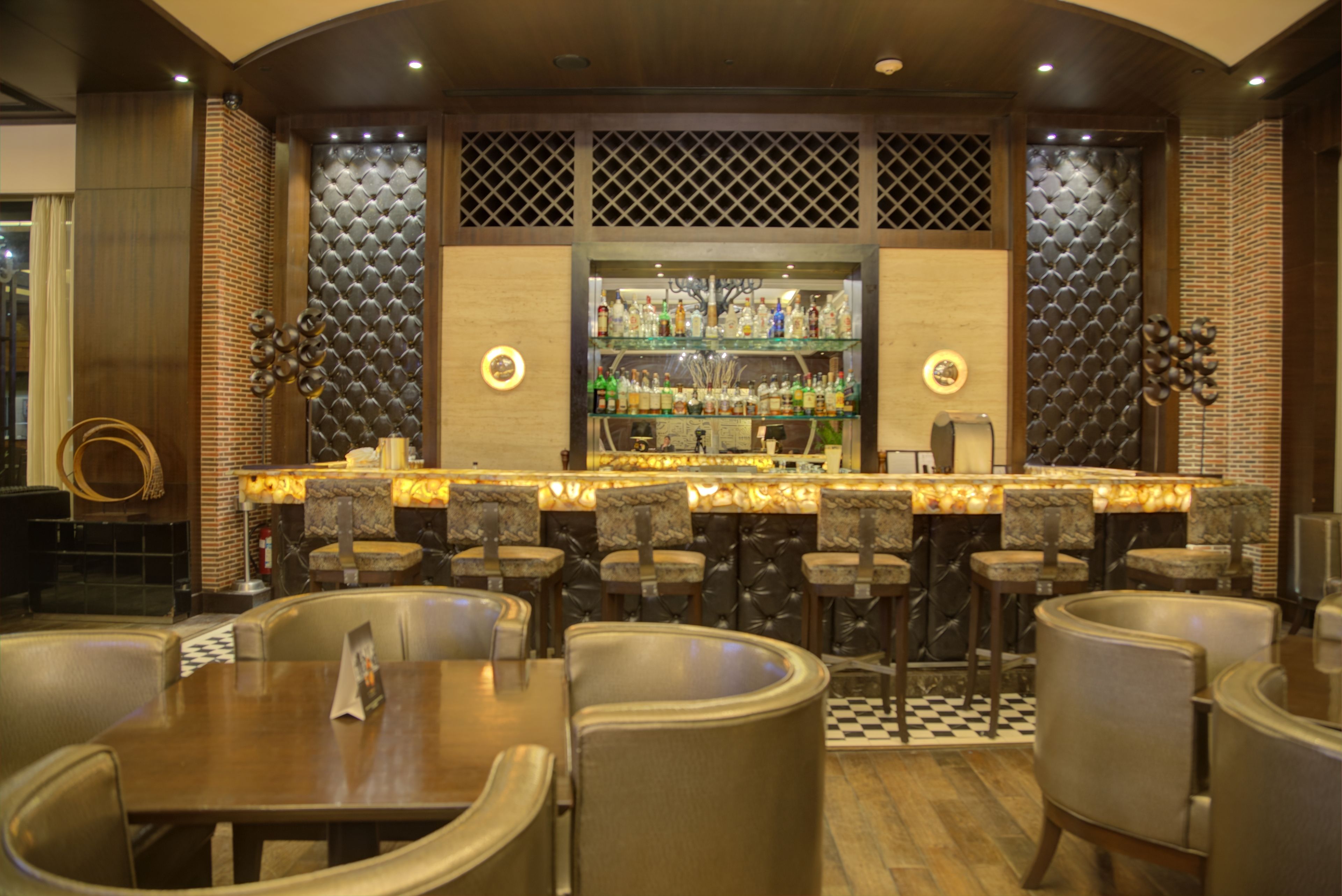 A bar area with multiple seating options, a well-lit bar counter, and a variety of bottles on shelves.