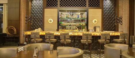 A bar area with multiple seating options, a well-lit bar counter, and a variety of bottles on shelves.