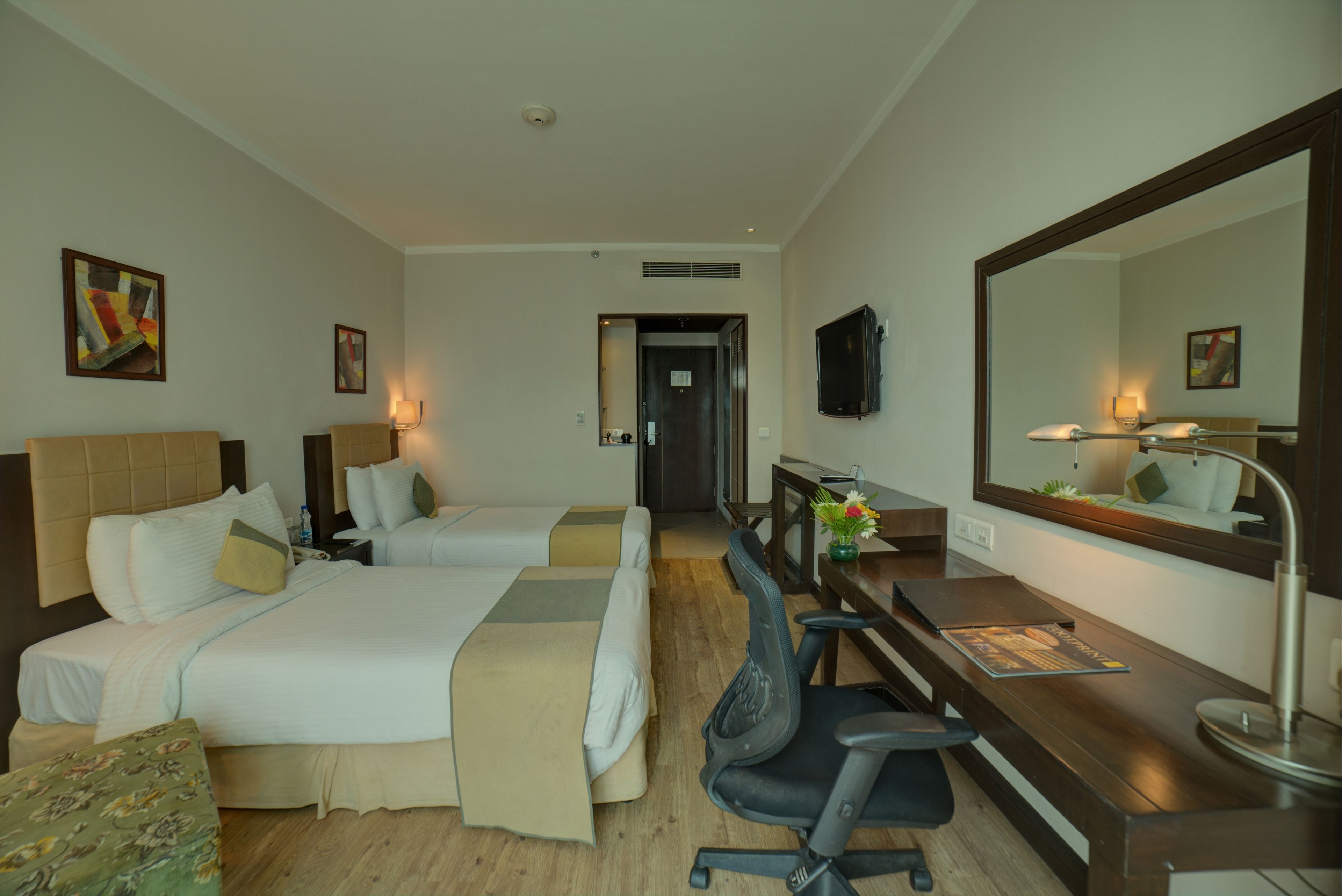 A hotel room with two beds, a desk, a chair, a TV, and a large mirror.