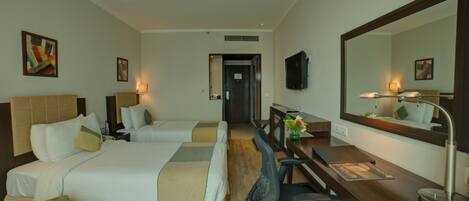A hotel room with two beds, a desk, a chair, a TV, and a large mirror.